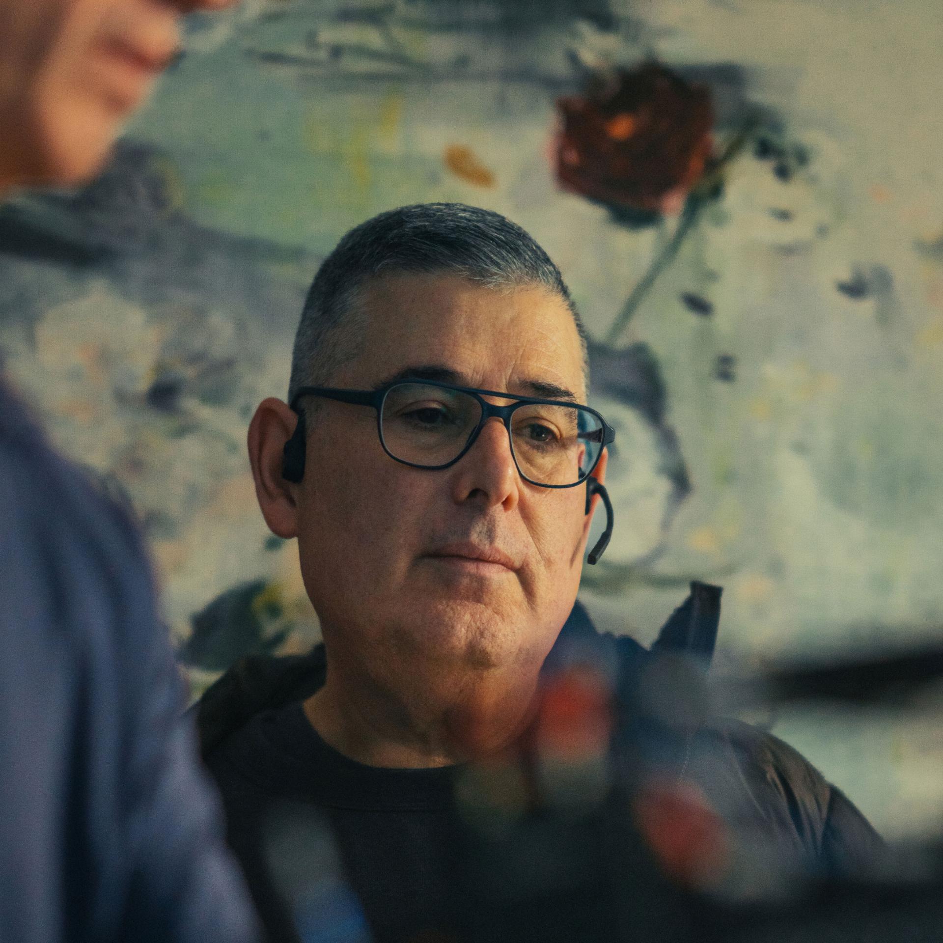 Man wearing glasses and a headset, focused on equipment, with a blurred artistic background.