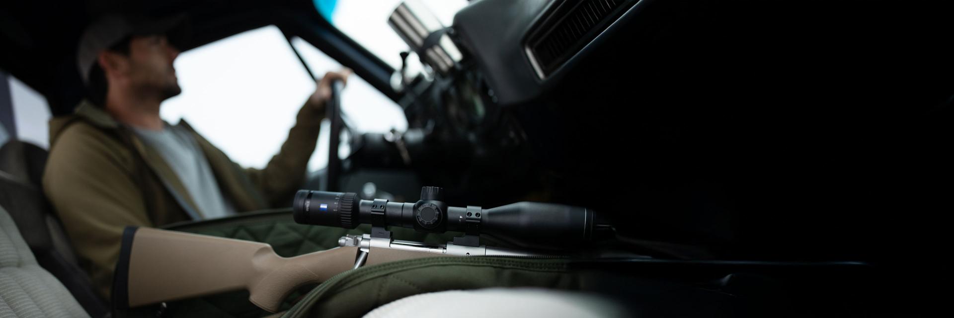 Sunglasses with ZEISS lenses lying on a blue table, reflecting a smiling woman, next to a smartphone and a glass of water.