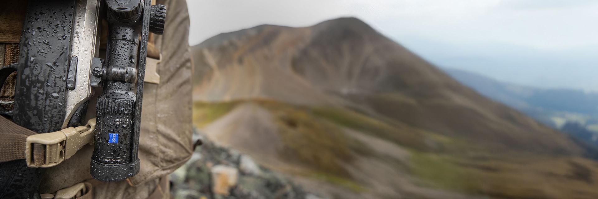 Sunglasses with ZEISS lenses lying on a blue table, reflecting a smiling woman, next to a smartphone and a glass of water.