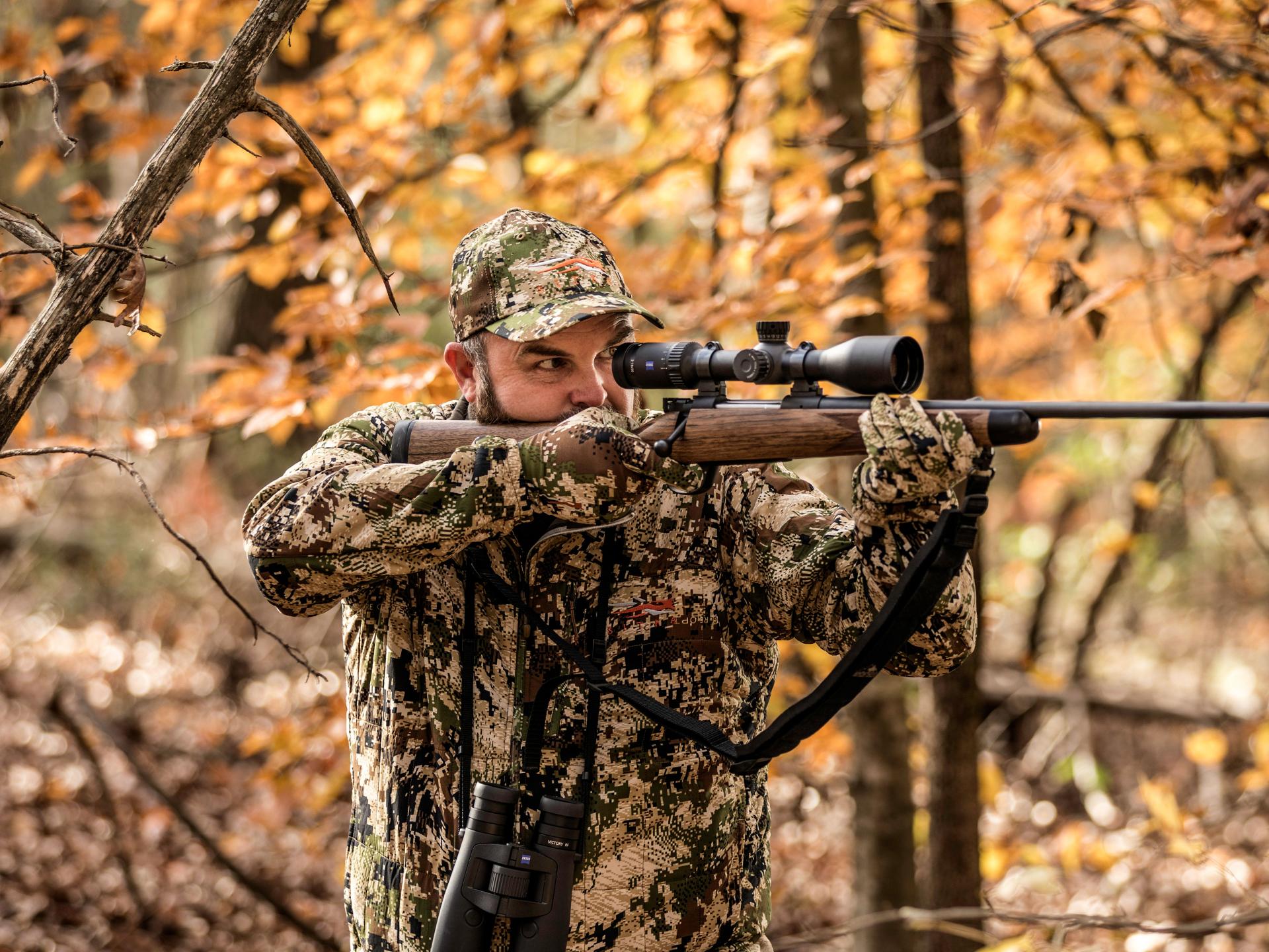 A hunter in autumn forest surroundings shoulders his rifle with a ZEISS Conquest V6 riflescope, ensuring reliable precision for all hunting situations.
