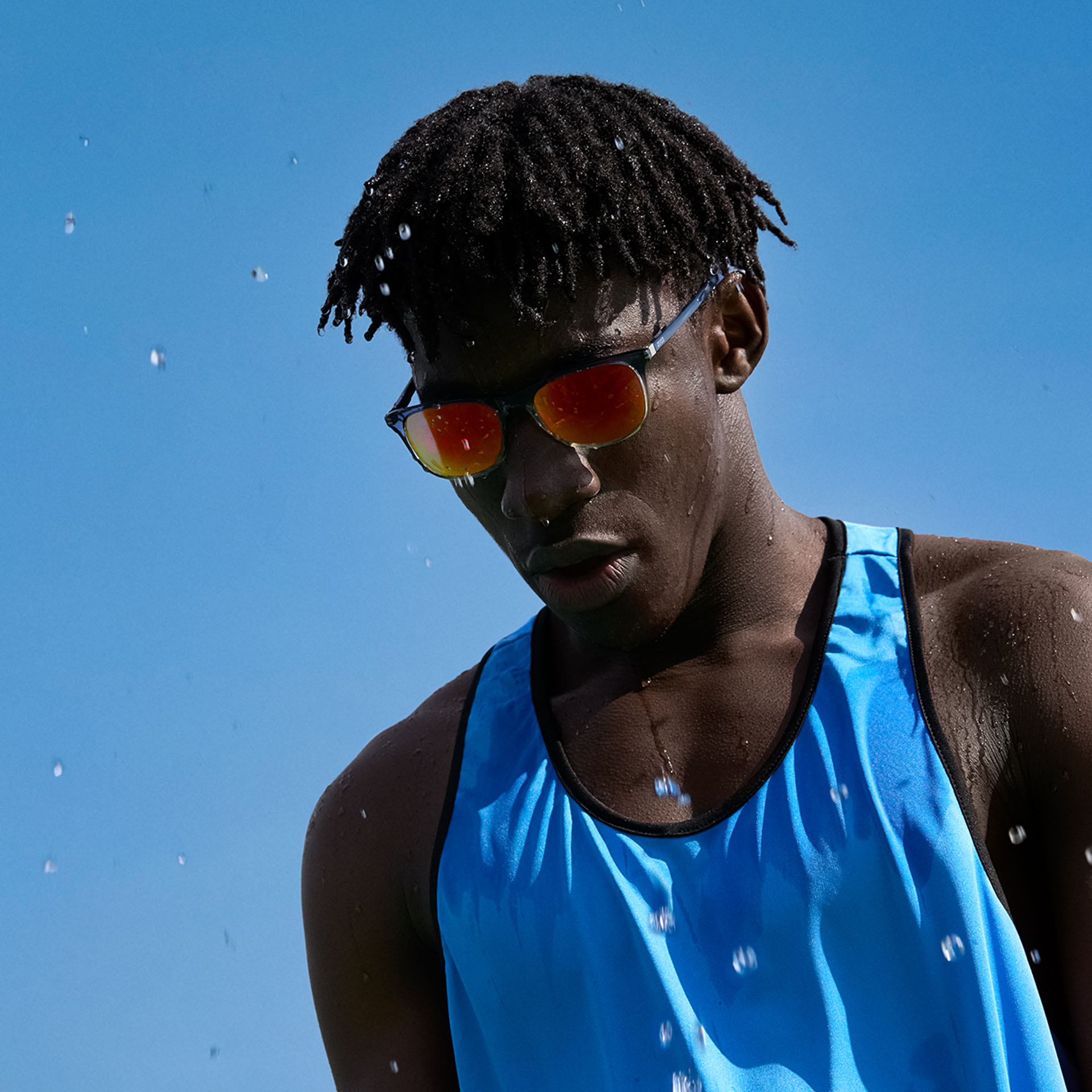 Un joven con ropa deportiva y lentes de sol de alto rendimiento de ZEISS en tono marrón anaranjado ante un cielo azul.