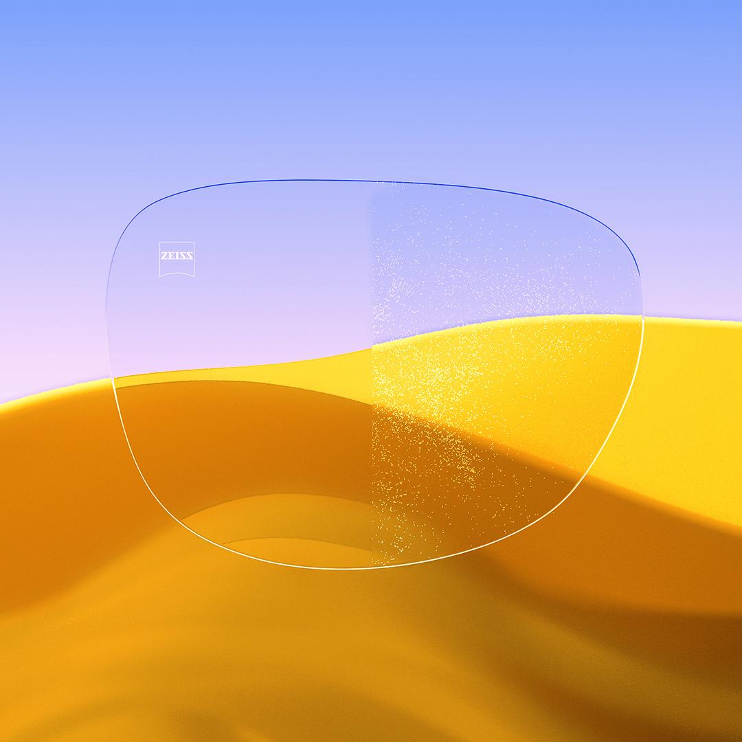 Una lente partida con un lado transparente con ZEISS DuraVision Gold UV y un lado con polvo sobre la lente.