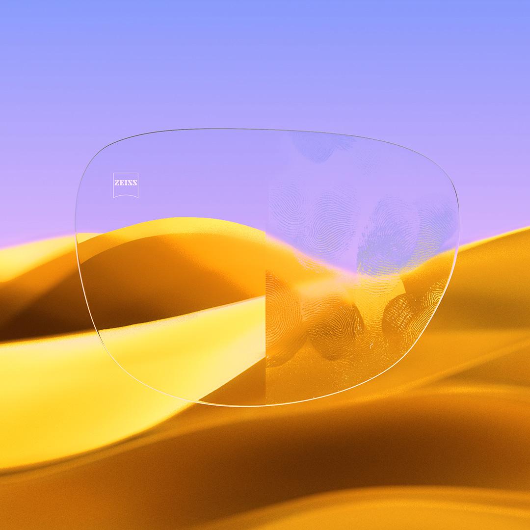 Una lente partida con un lado transparente con ZEISS DuraVision Gold UV y un lado con huellas sobre la lente.