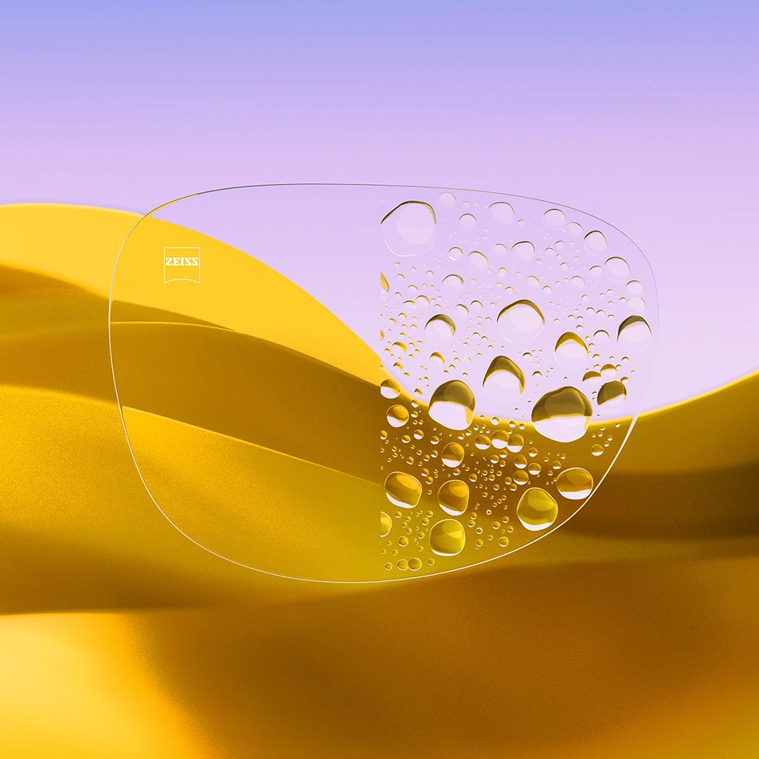 Una lente partida con un lado transparente con ZEISS DuraVision Gold UV y un lado con gotas de agua sobre la lente.