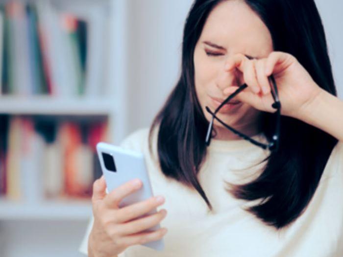 Una imagen muestra a una mujer de unos 30 años mirando su teléfono mientras se frota los ojos.