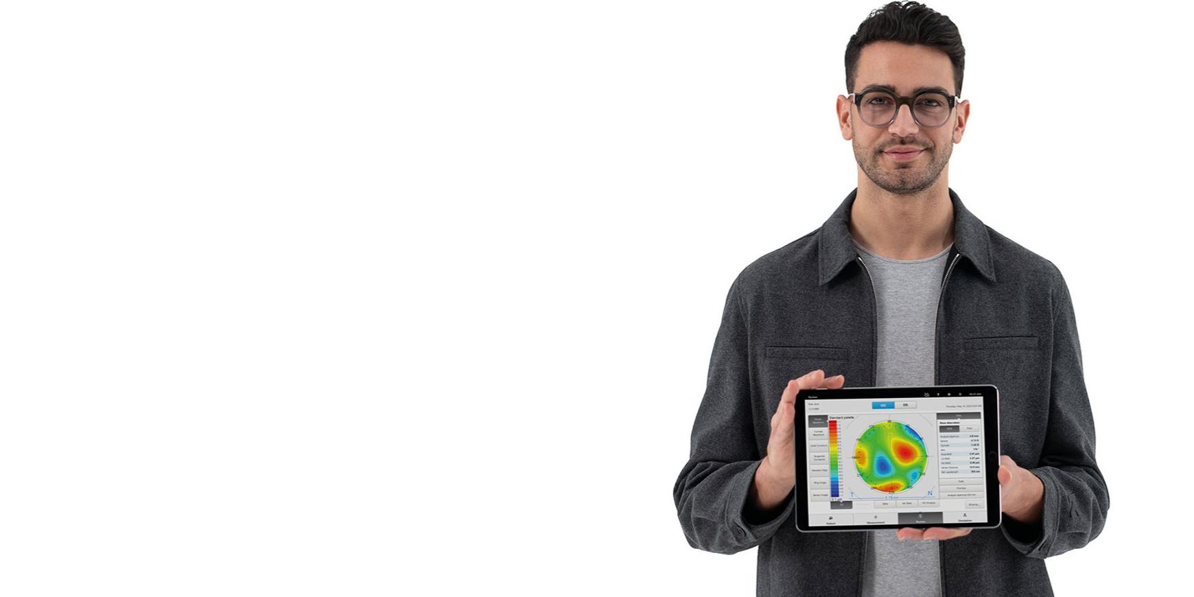 Un joven con lentes ZEISS mira a la cámara y sostiene un iPad que muestra información previa para una refracción subjetiva precisa.