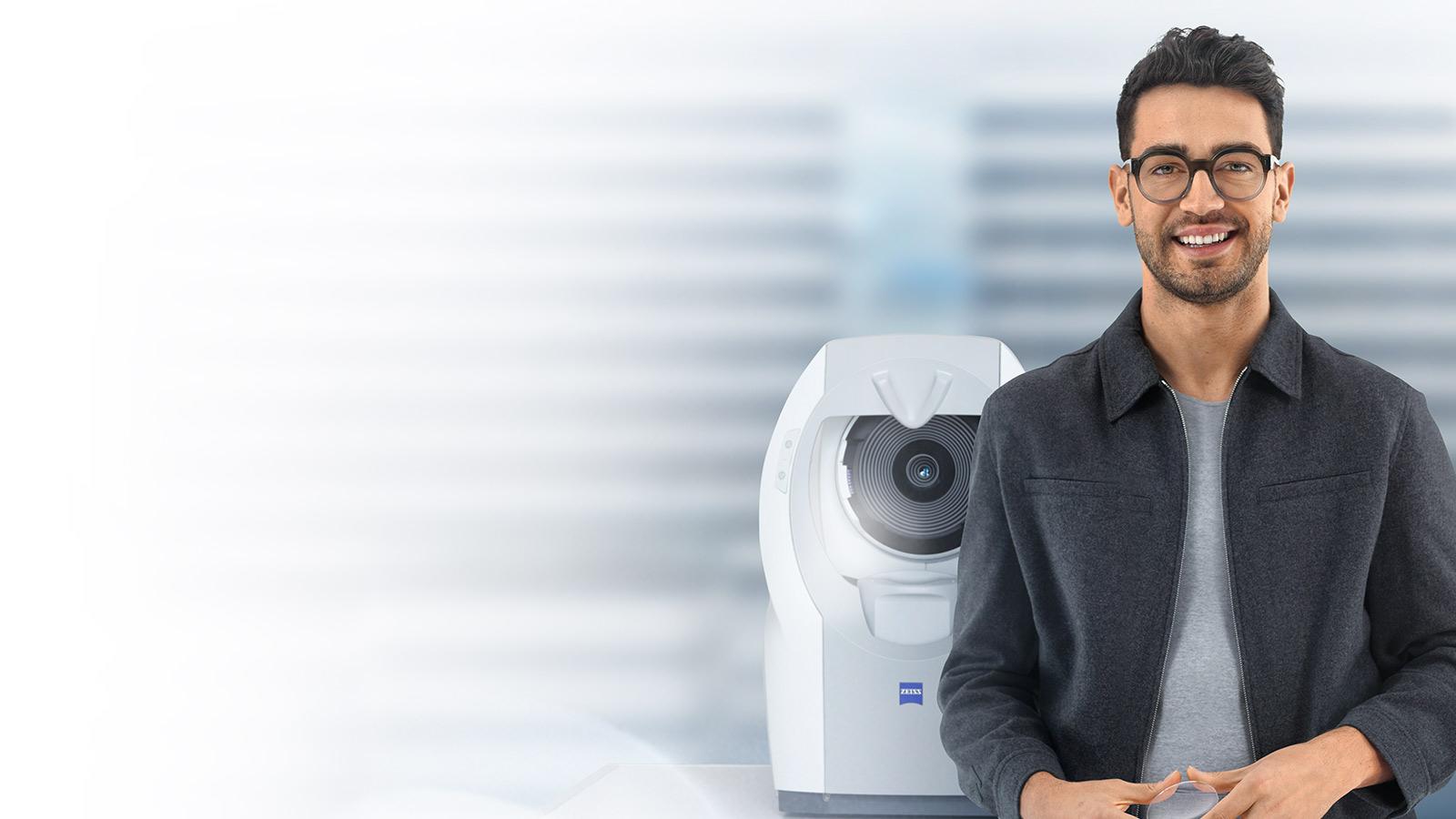 Un joven de pelo corto oscuro con lentes ZEISS SmartLife sonriendo a la cámara. De fondo, un ZEISS i.Profiler plus.