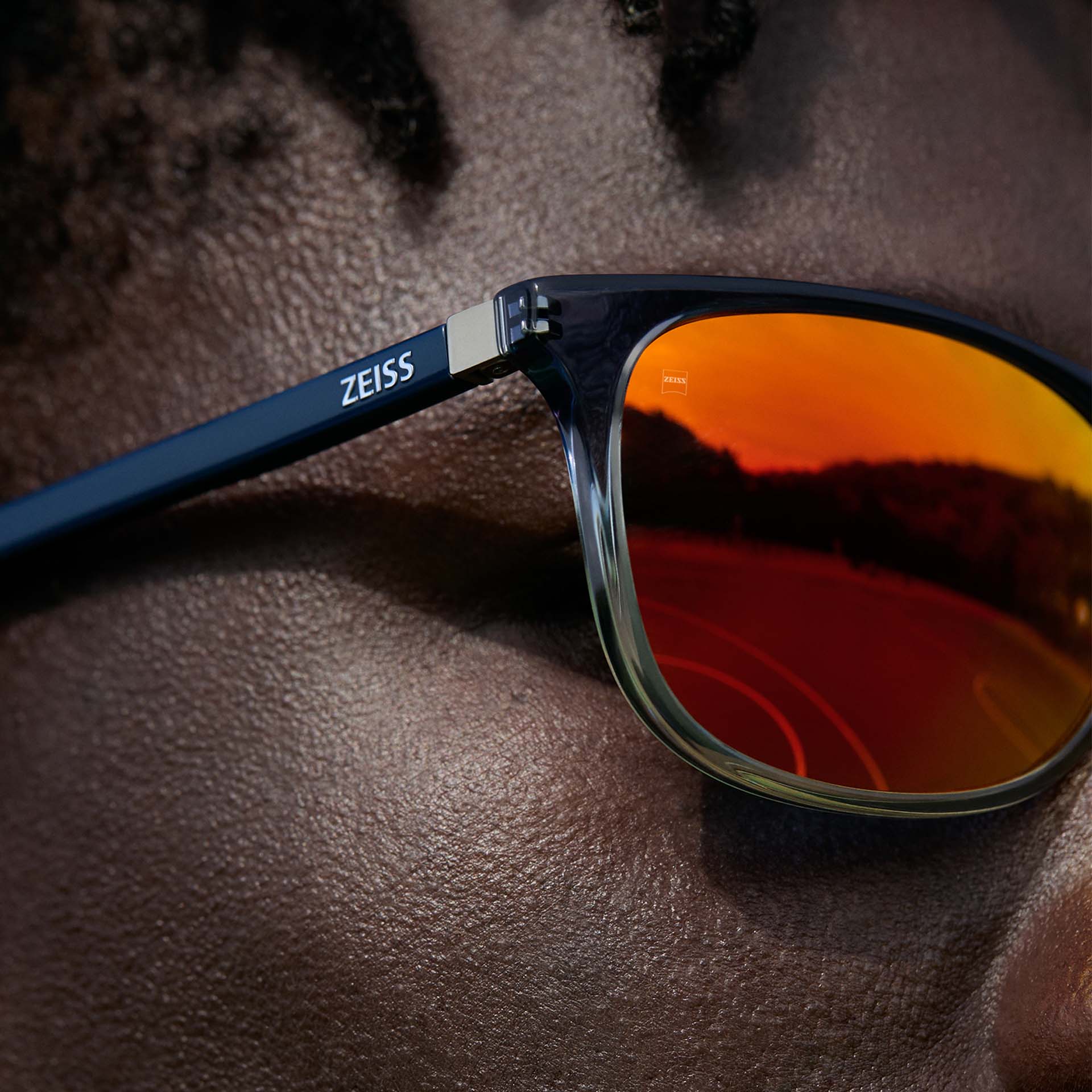 Primer plano de un hombre con gafas de sol ZEISS con tratamiento DuraVision Mirror UV de ZEISS en color naranja.