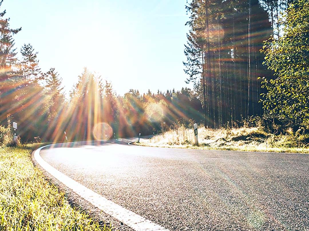 Imagen con una barra deslizante en la que una mitad muestra una carretera en pleno bosque muy iluminada por el sol y la otra mitad muestra la misma carretera con menor deslumbramiento y mayor contraste, lo que resalta el efecto de las lentes de sol polarizadas.