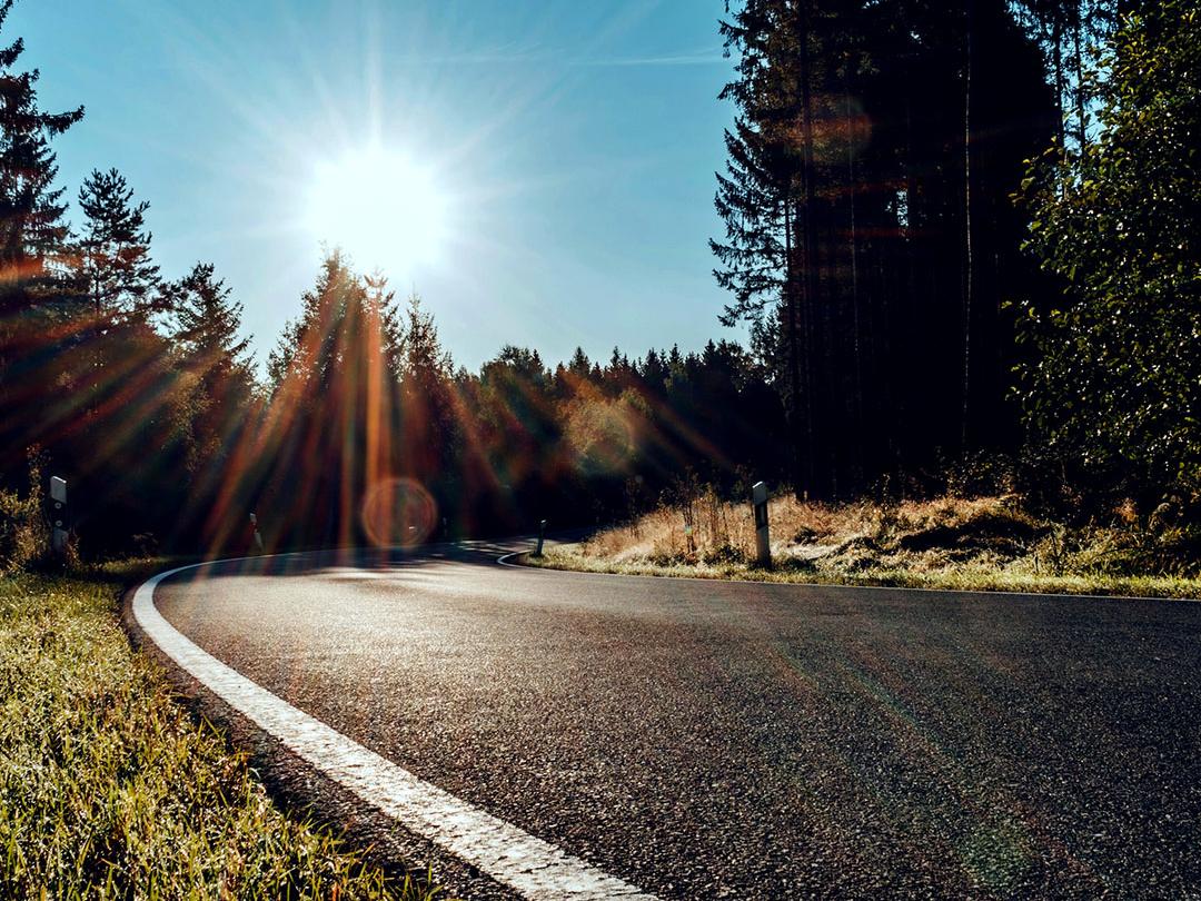 Imagen con una barra deslizante en la que una mitad muestra una carretera en pleno bosque muy iluminada por el sol y la otra mitad muestra la misma carretera con menor deslumbramiento y mayor contraste, lo que resalta el efecto de las lentes de sol polarizadas.