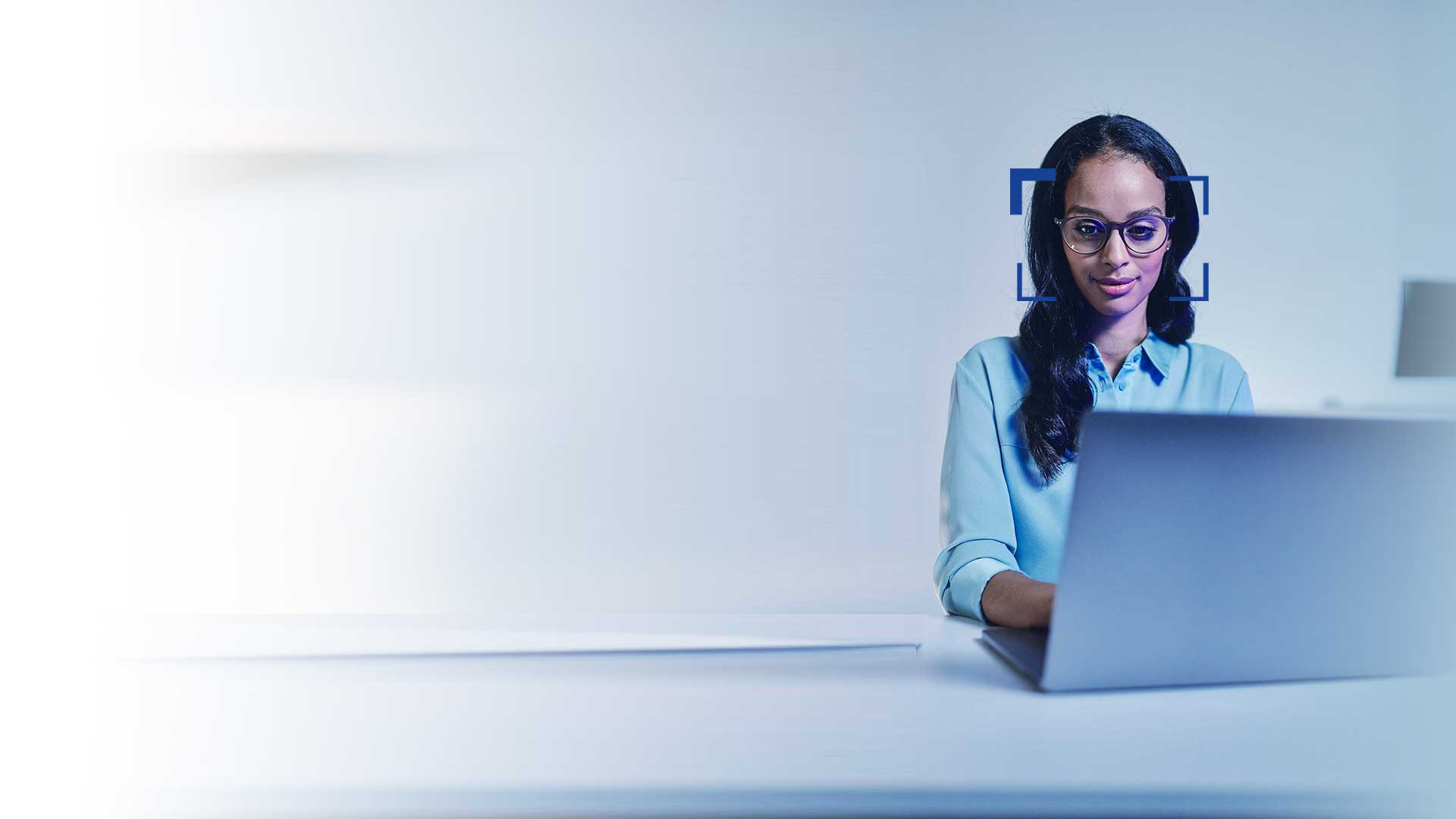 Woman with black hair and glasses watches smiling into a laptop