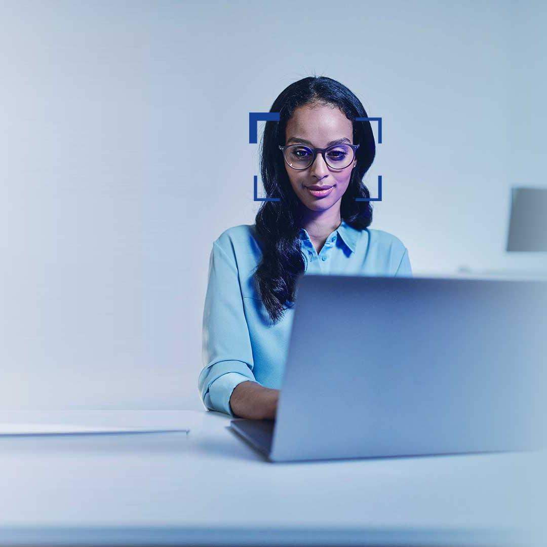 Mujer con cabello negro y gafas sonríe hacia el portátil