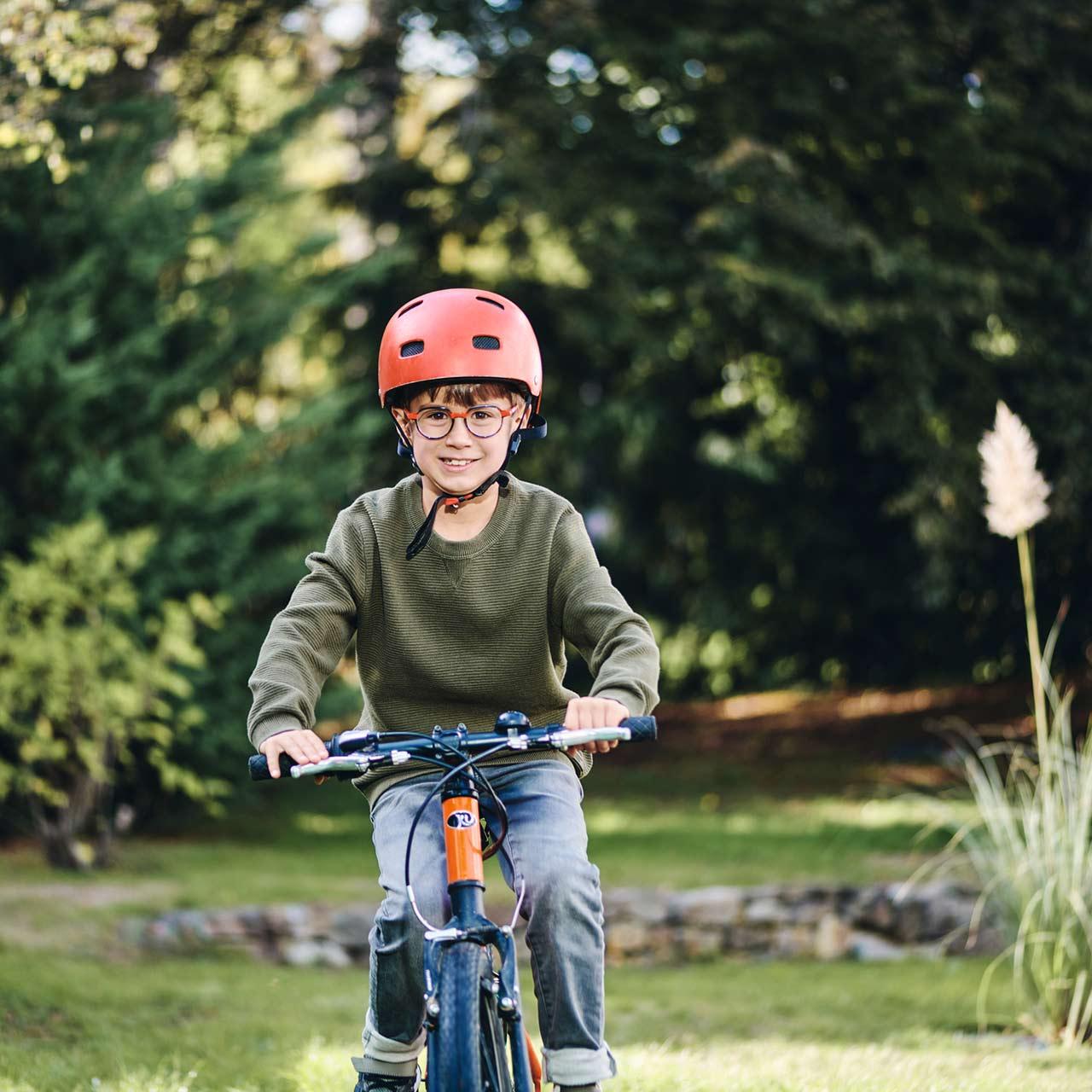 Niño con gafas montando en bici al aire libre con una sonrisa
