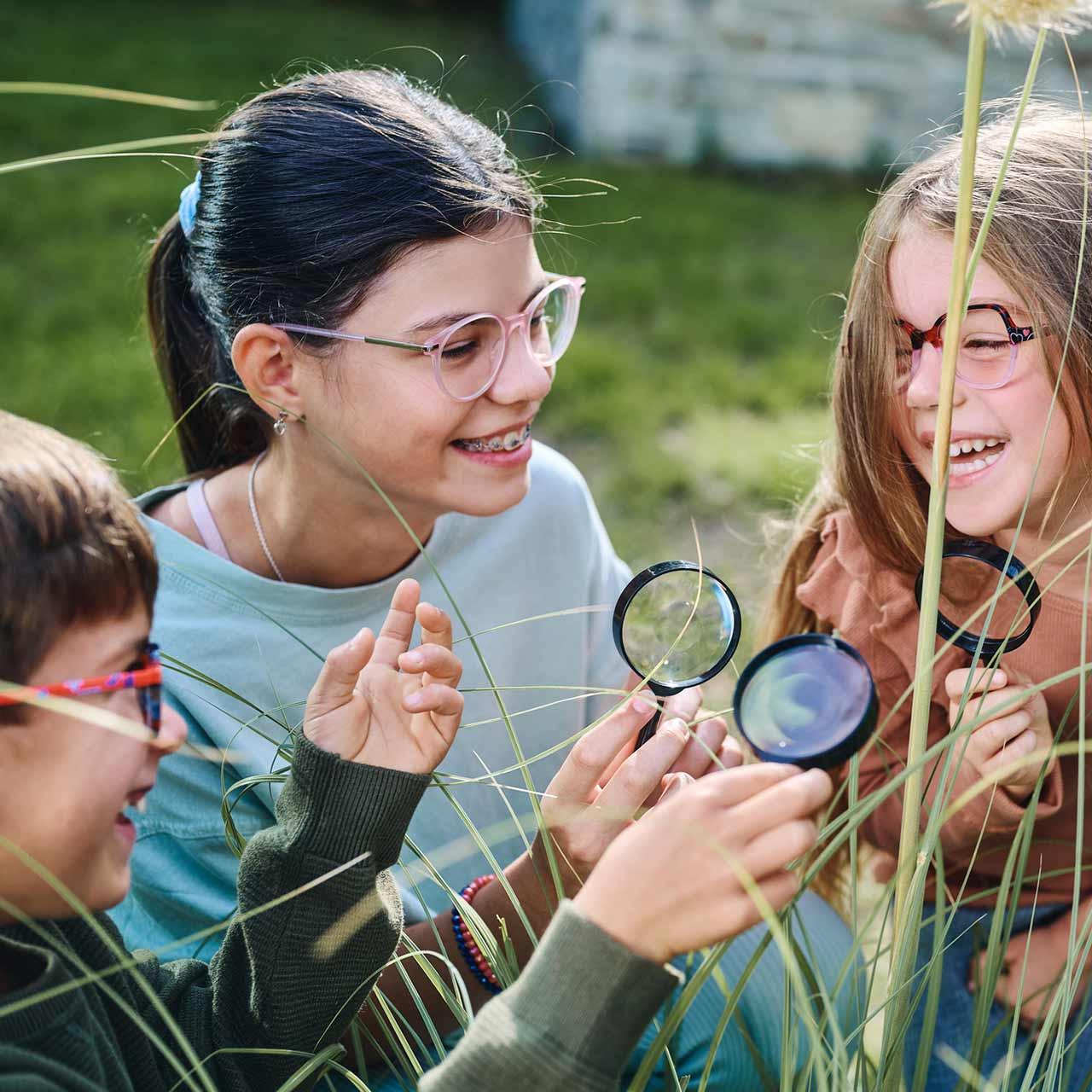 Grupo de niños con gafas y lupas jugando y riendo al aire libre