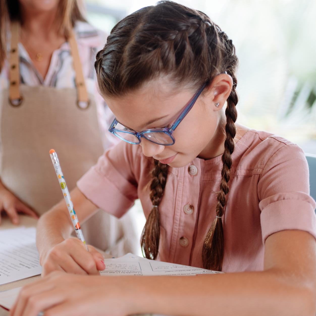 Niña con gafas escribiendo con un bolígrafo