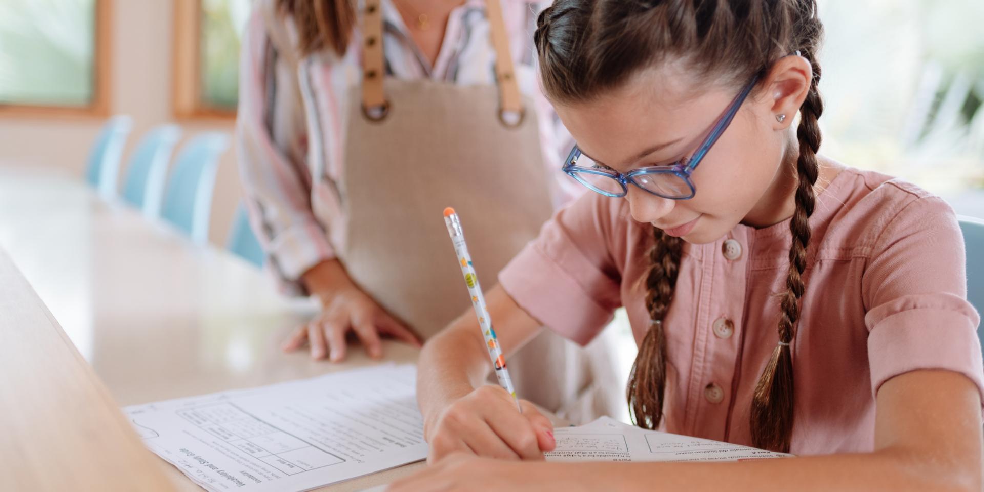 Niña con gafas escribiendo con un bolígrafo
