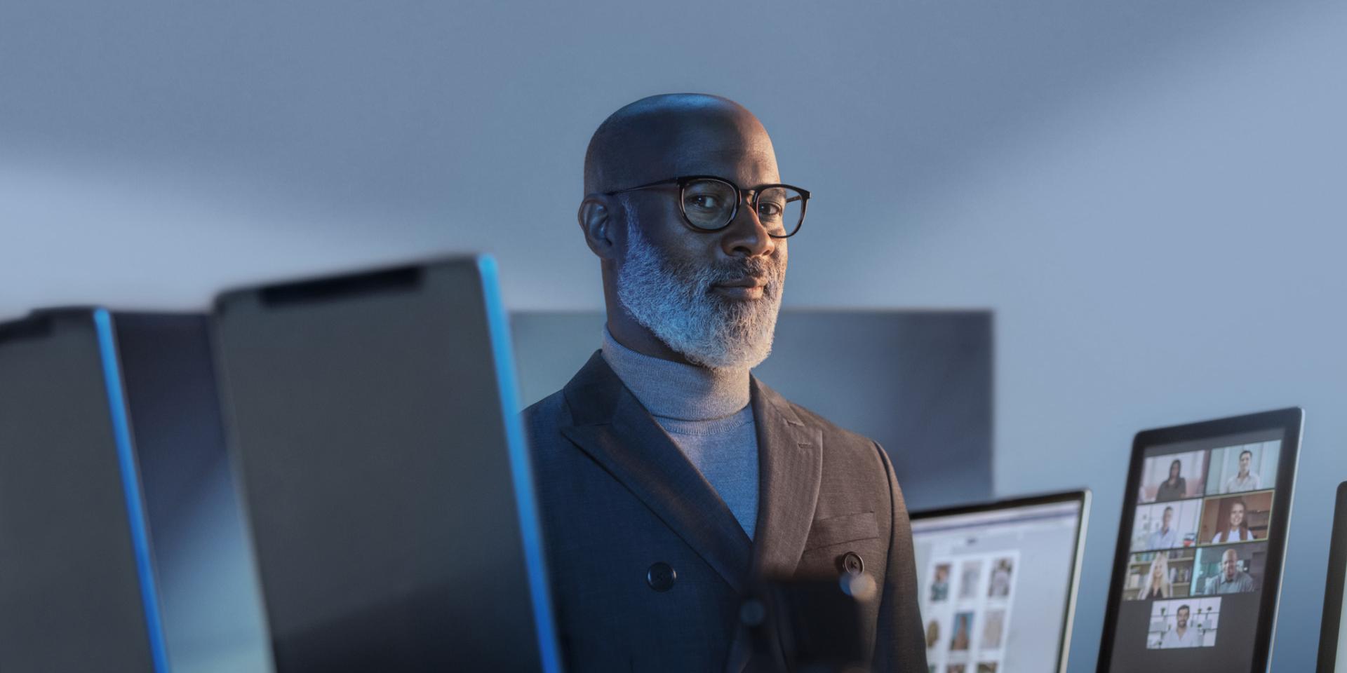 Hombre sonriente rodeado de dispositivos digitales usando gafas con ZEISS BlueGuard para protegerse contra la luz azul.