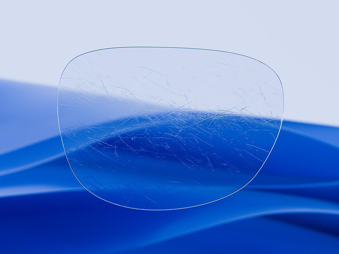Imagen dividida que muestra una lente ZEISS en una mitad, caracterizada por su claridad y limpieza, y una lente convencional rayada en la otra mitad, lo que resalta el contraste en relación con la durabilidad. 