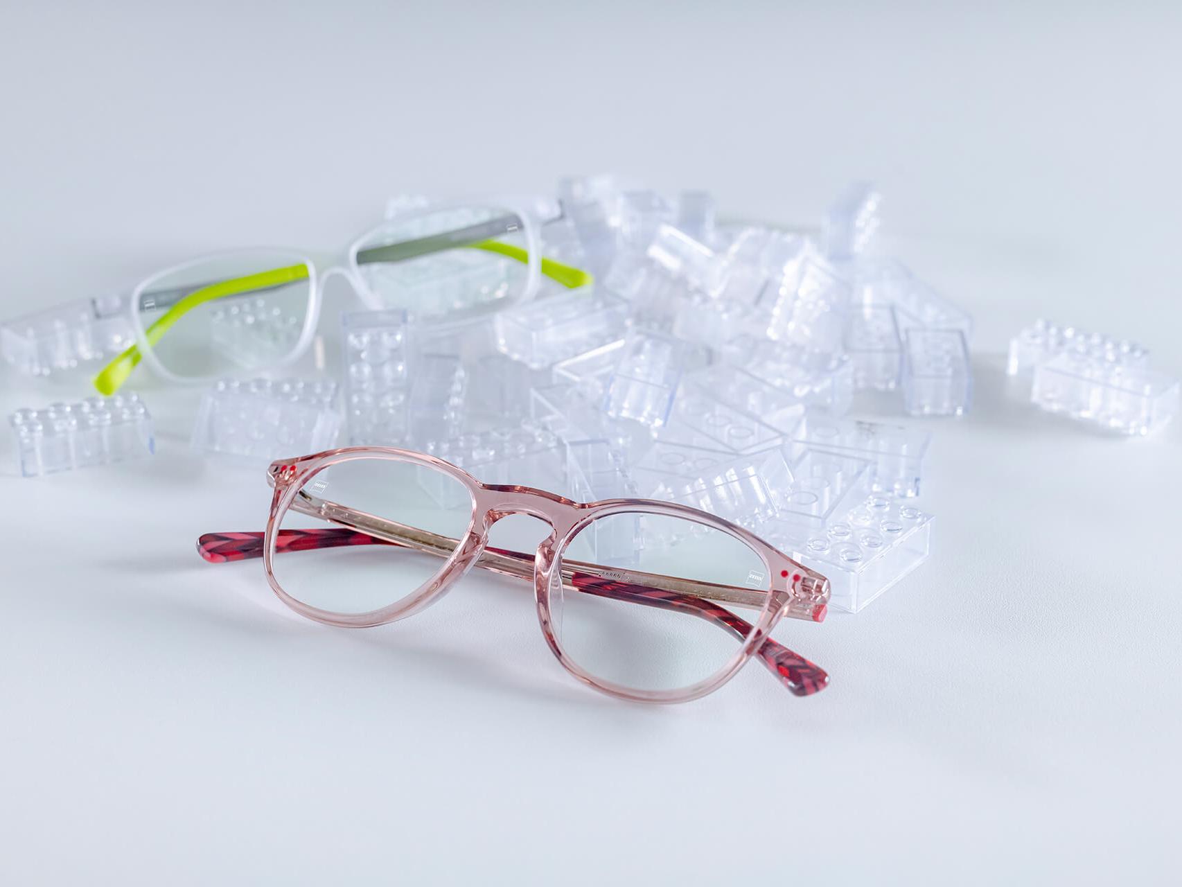 Dos pares de gafas infantiles con lentes ZEISS y protectores DuraVision® para niños. Las gafas se colocan entre ladrillos infantiles transparentes.
