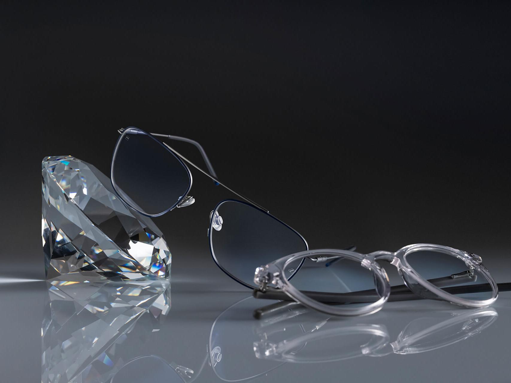 Dos pares de gafas con lentes ZEISS y el protector ZEISS más duro hasta la fecha: DuraVision® Platinum. Un par de gafas apoyado en un cristal, el otro sobre el suelo. Ambas tienen lentes transparentes sin reflejos azulados.