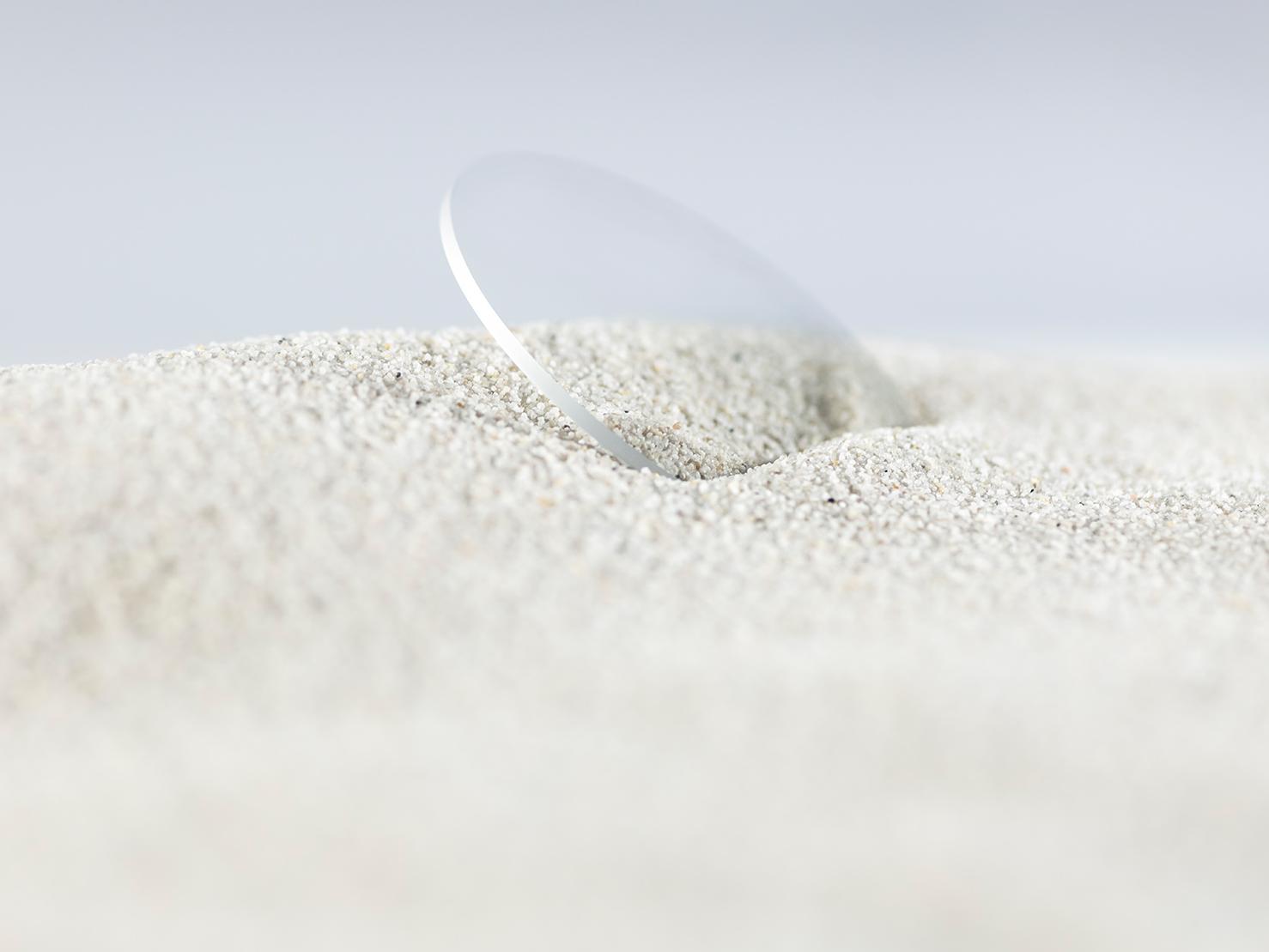 Una lente ZEISS con un protector duradero se cubre de arena gruesa, pero no se raya.