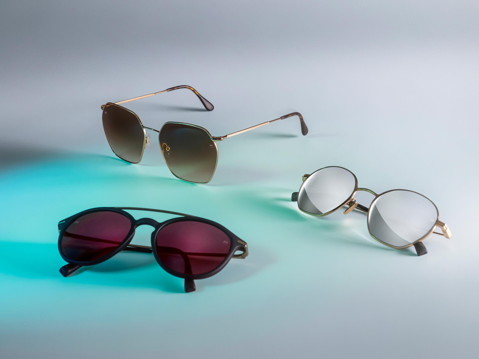Tres pares de gafas de sol con lentes de gafas de sol ZEISS de distintos colores, con protectores DuraVision Sun, DuraVision Mirror y Flash Mirror, visibles sobre un fondo blanco con reflejo de luz azul.