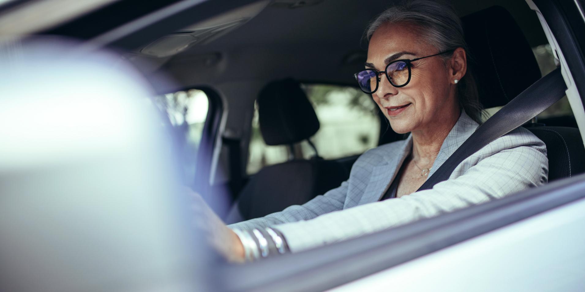Una mujer madura en un coche lleva gafas con lentes ZEISS DriveSafe.