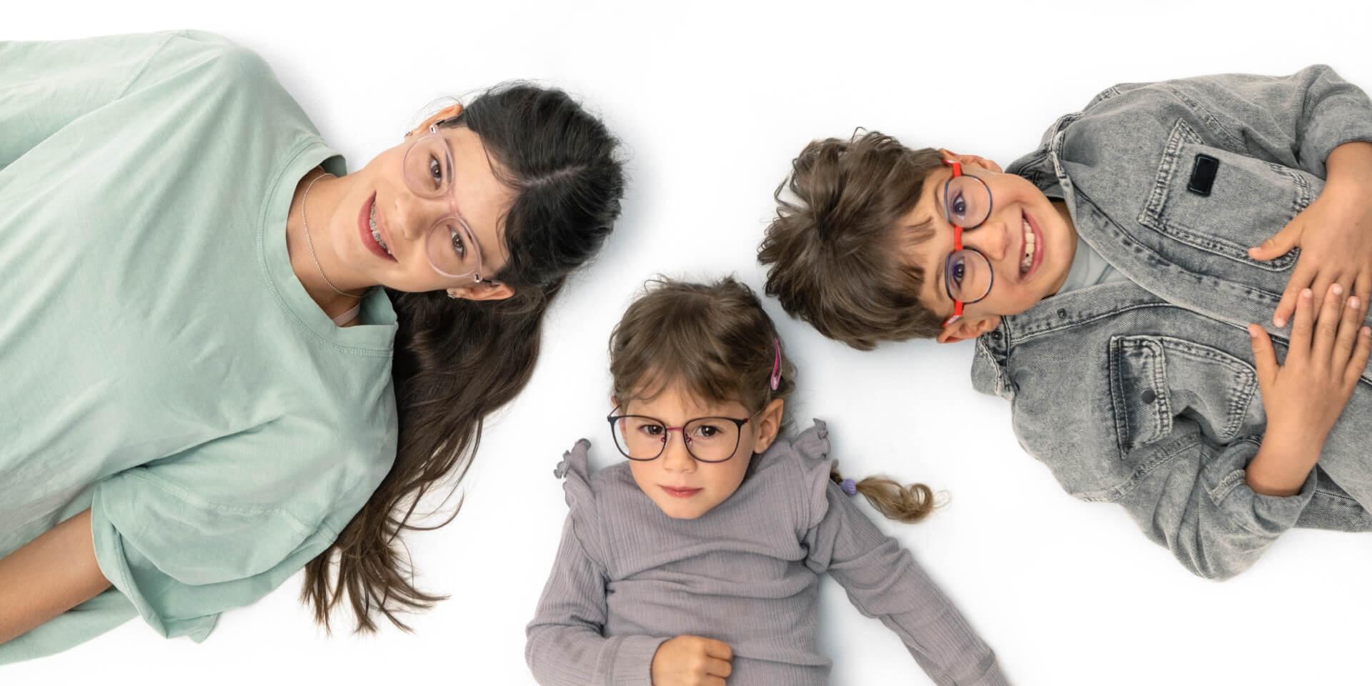 Un adolescente y dos niños más pequeños tumbados en el suelo con lentes para la miopía de ZEISS.