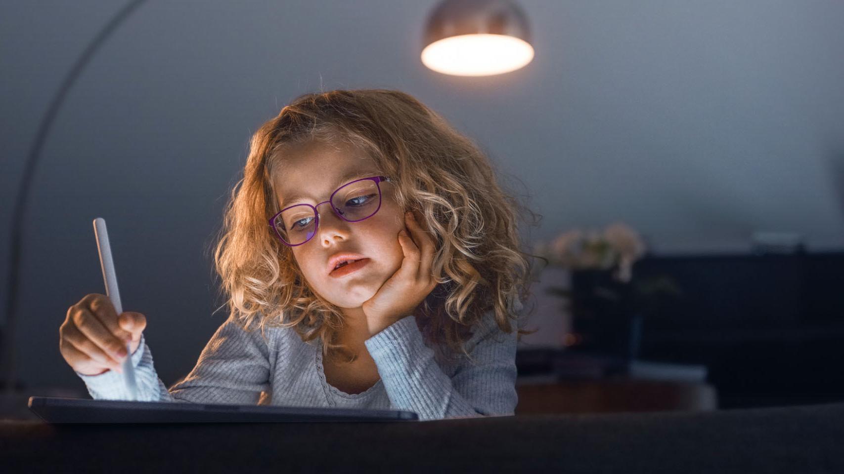 Niña en un salón oscuro mirando una tableta.