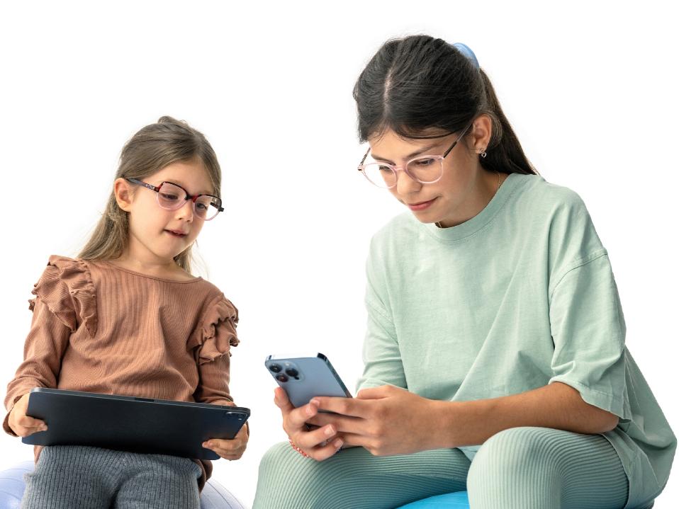 Dos niñas mirando dispositivos digitales a la distancia sugerida de más de 20 cm.