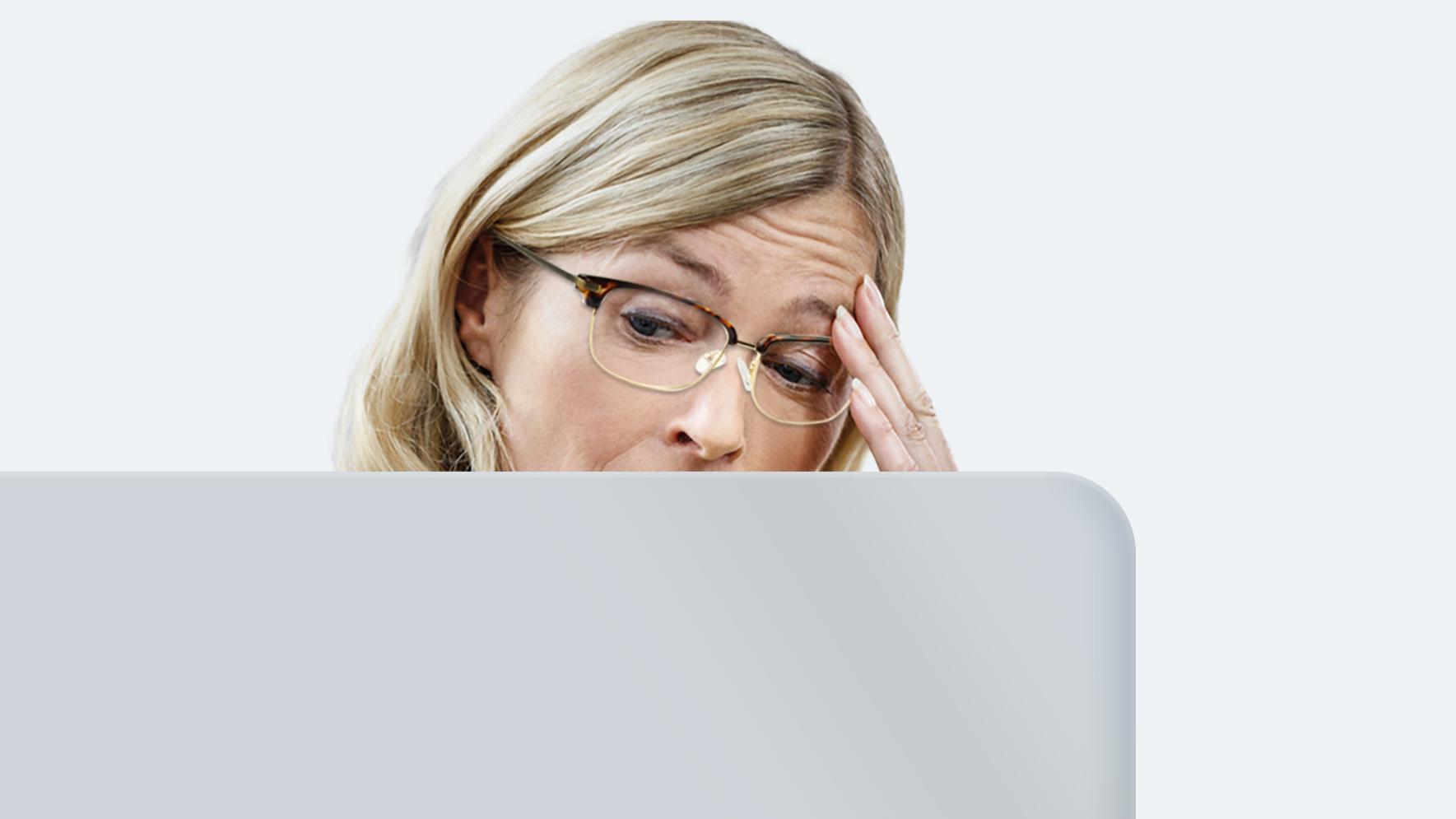Una mujer de mediana edad con melena larga rubia y gafas de lejos sufre fatiga ocular porque sus lentes no están hechas para mirar una pantalla durante todo el día.