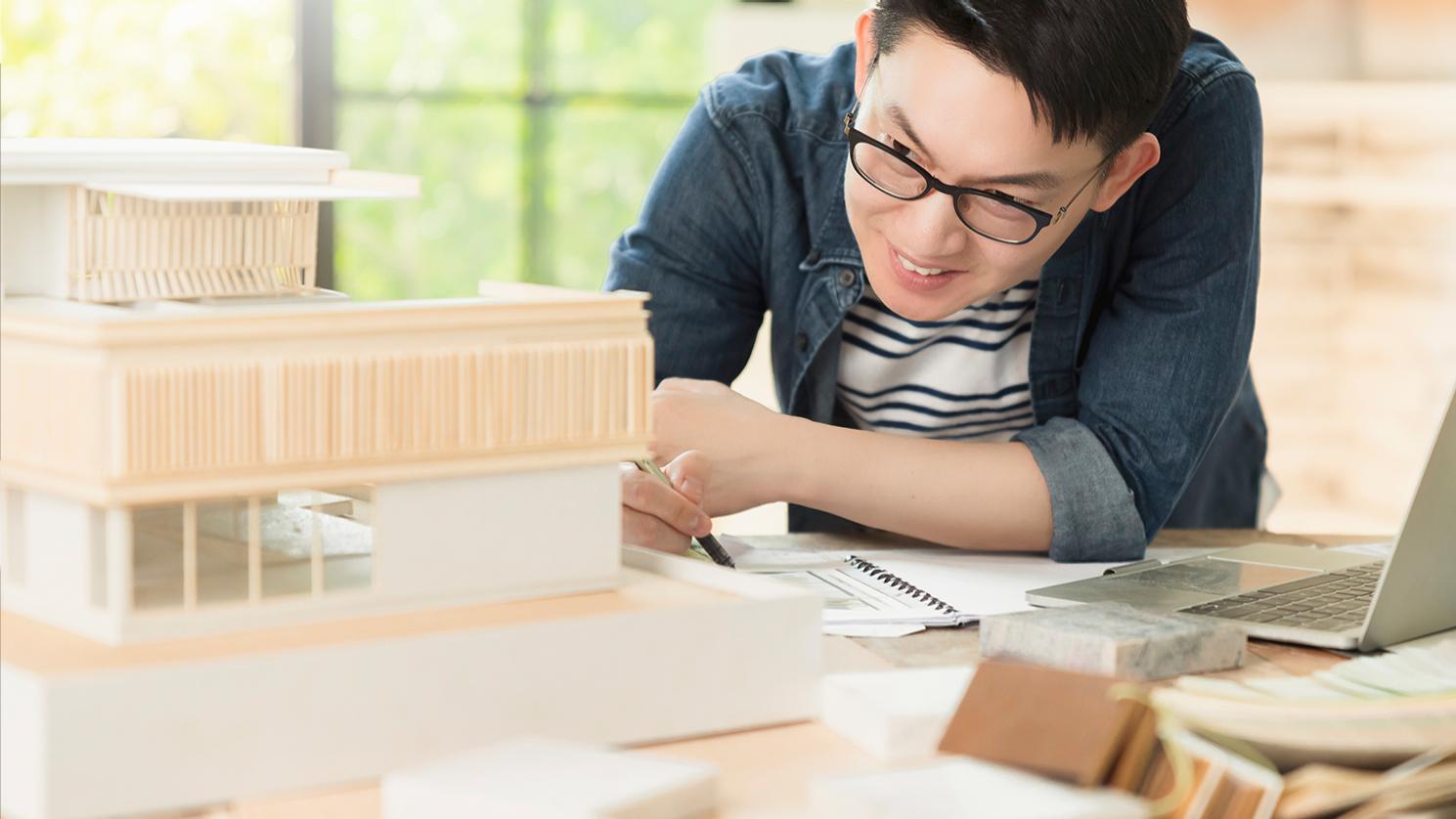 Hombre de mediana edad con pelo corto negro y gafas de oficina ZEISS Office para poder concentrarse en los detalles de un intrincado modelo arquitectónico. 