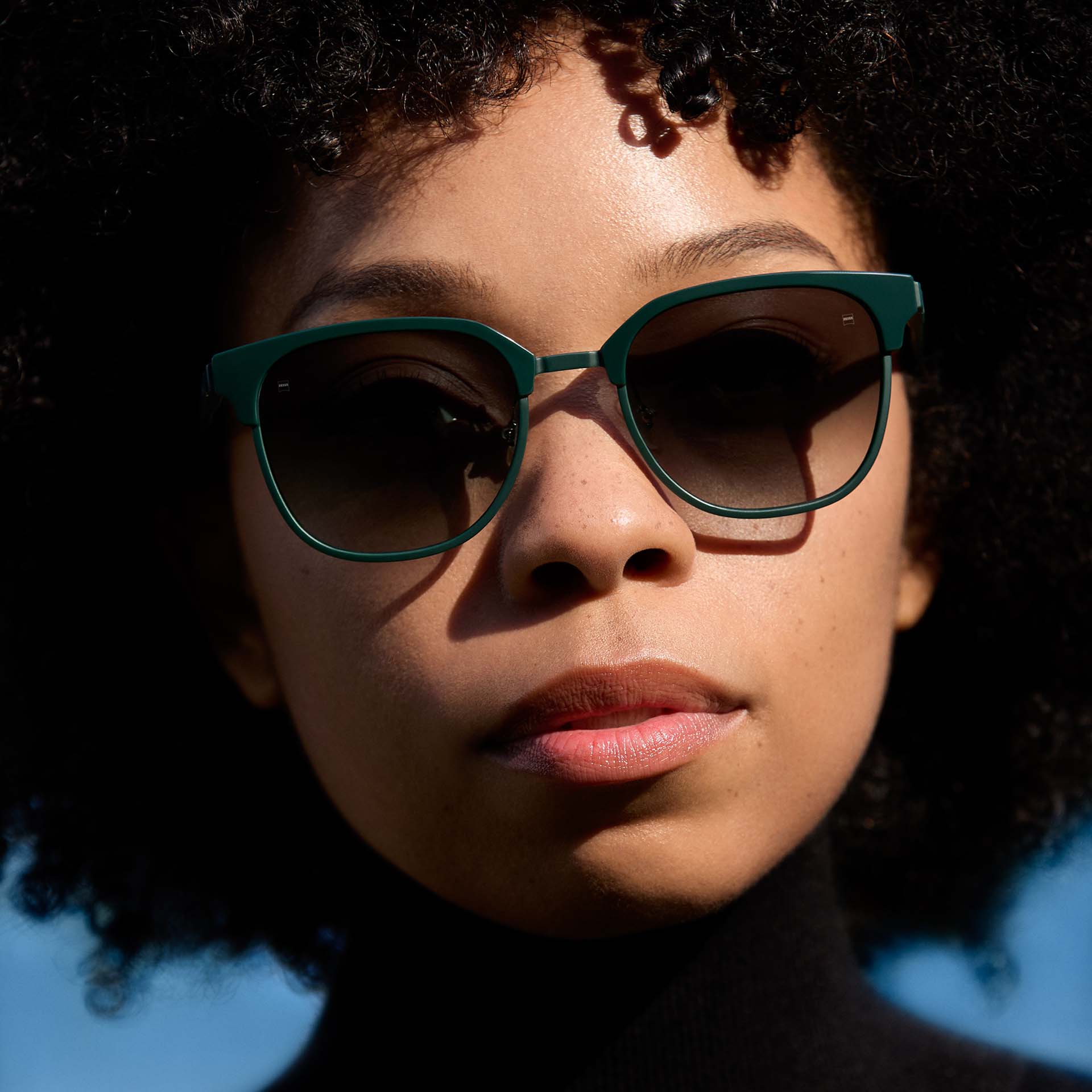 Una mujer con una montura verde y lentes de color degradado. 