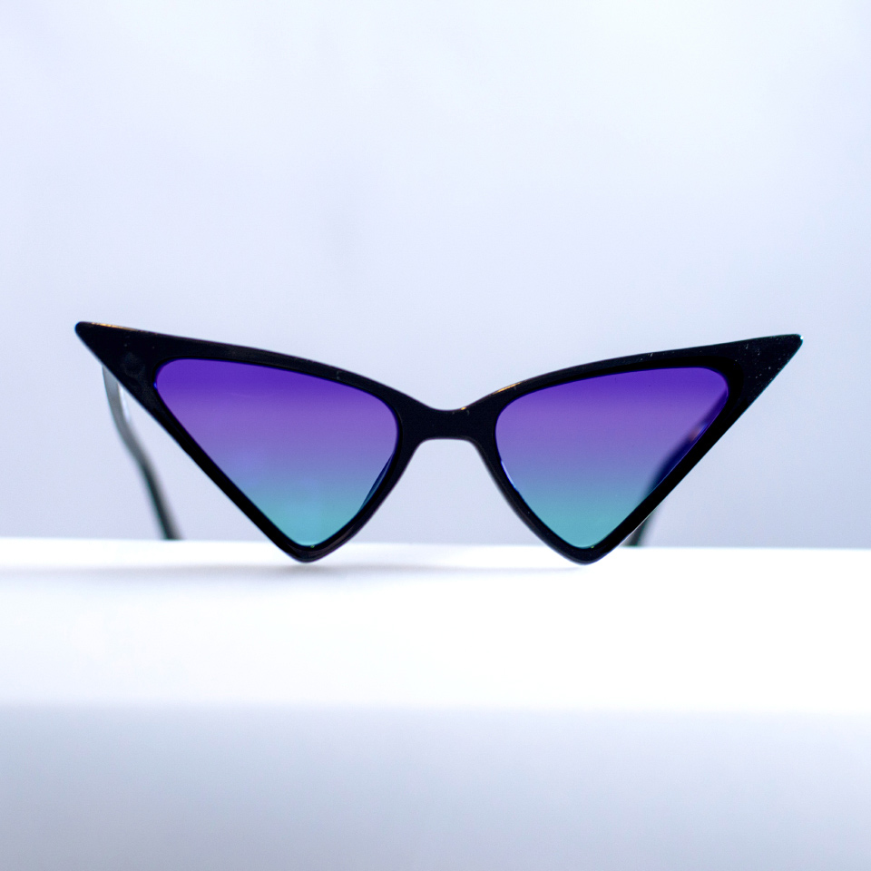 Gafas de sol tipo «cat eye» sobre una superficie blanca con degradado cian-morado