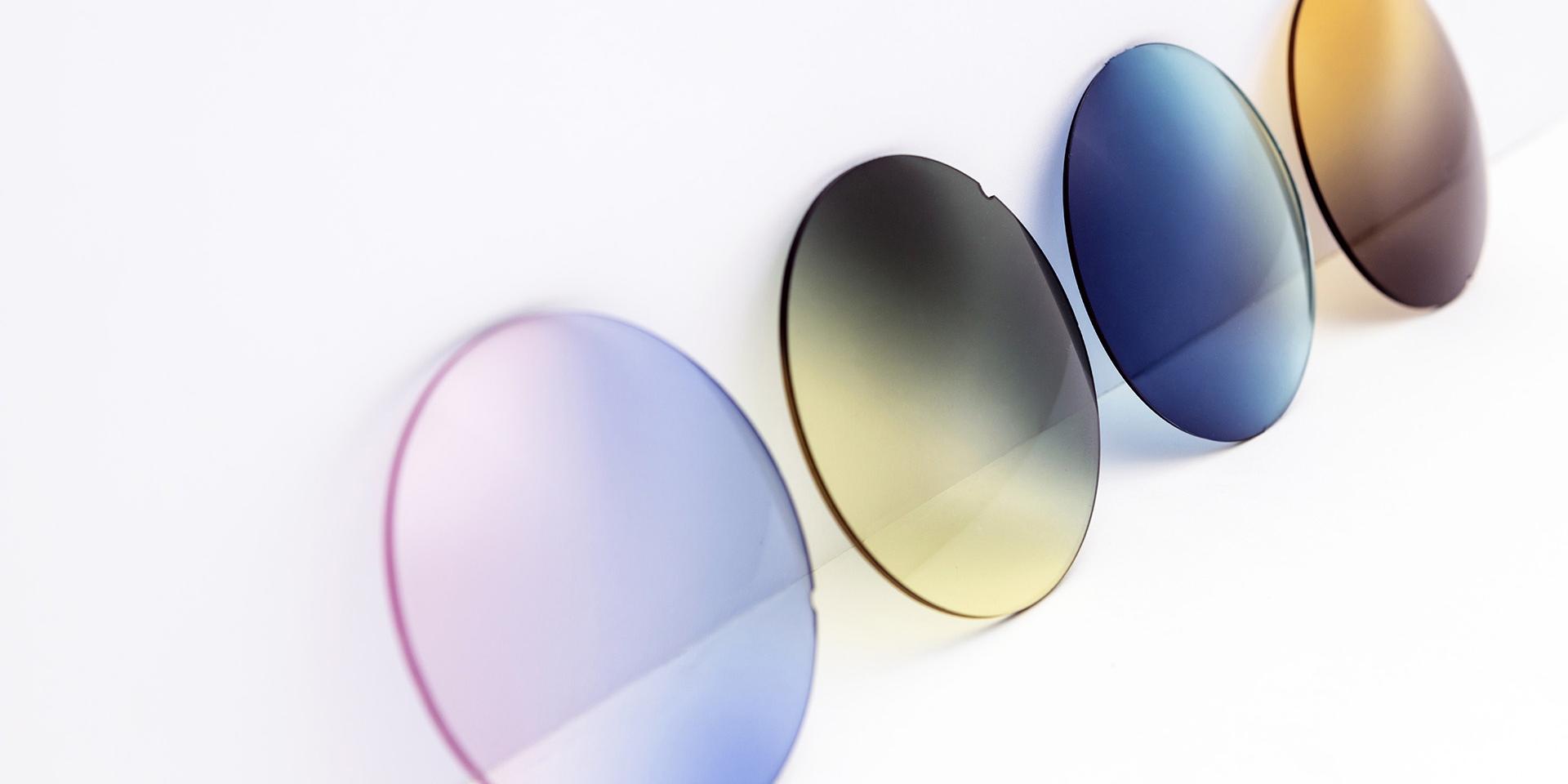 Lentes de sol de distintos colores sobre una superficie blanca: degradados rosa-morado, amarillo-gris, azul y marrón.