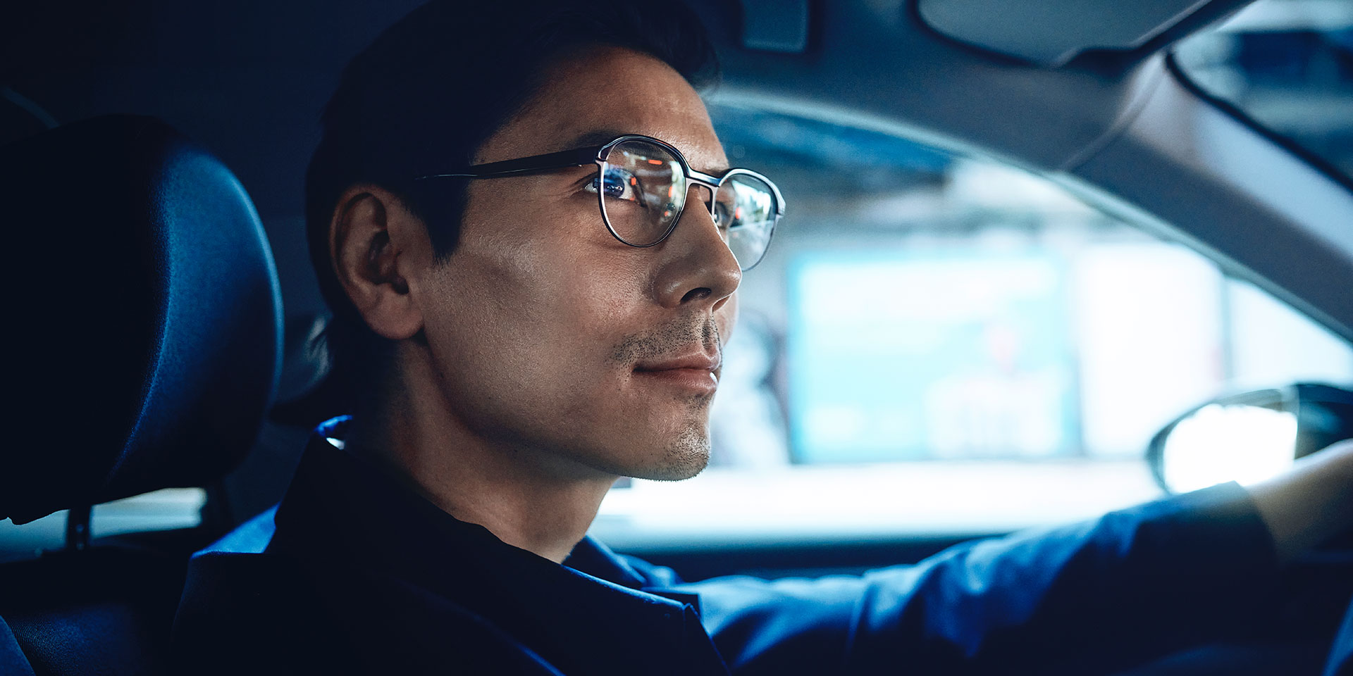 Hombre conduciendo un coche seguro de sí mismo y con una ligera sonrisa. Lleva lentes monofocales ZEISS DriveSafe.