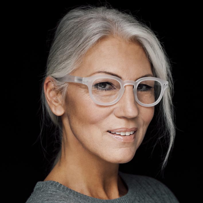 Mujer de pelo gris con montura blanca usando lentes progresivas ZEISS SmartLife. Escaneado geométrico del rostro que muestra la anatomía facial y las medidas de la montura.