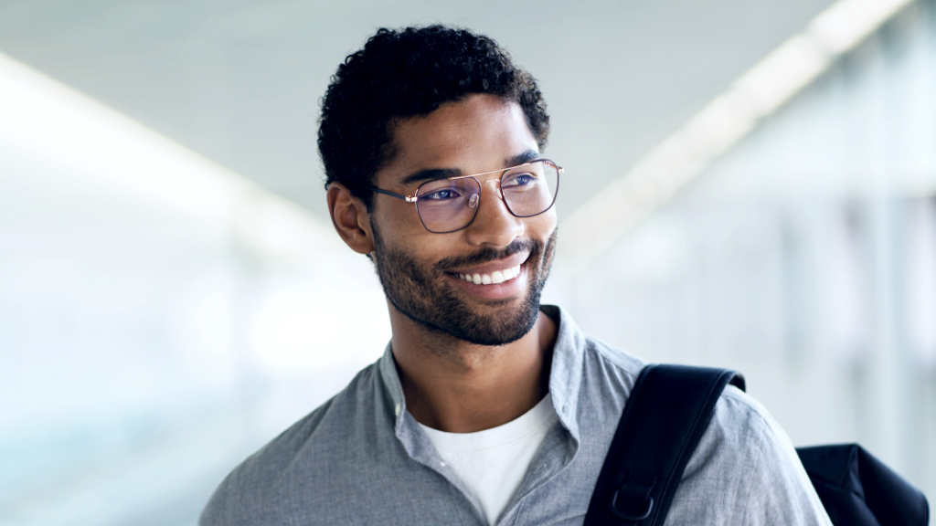 Un joven sonriente con una mochila al hombro lleva unas gafas ZEISS Digital SmartLife y mira hacia un lado.